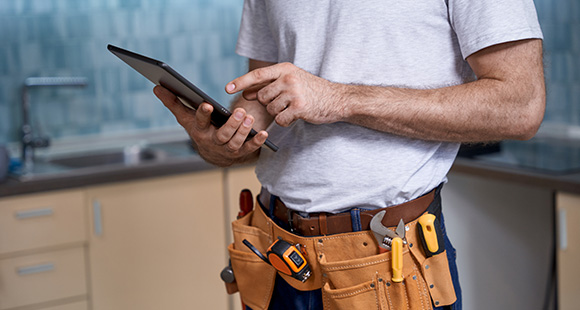 a person with a tool belt equipped using a tablet whilst stood in a kitchen