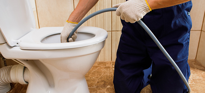 a plumber wearing wool gloves unclogging a toilet with a drainage system