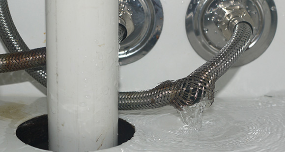 a broken pipe in a bathroom leaking water into a cupboard