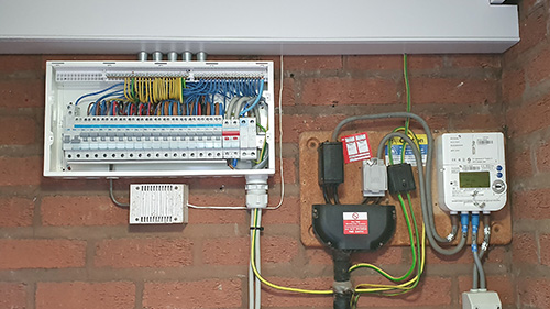a rewired fuse box connected to an electric meter on a brick wall