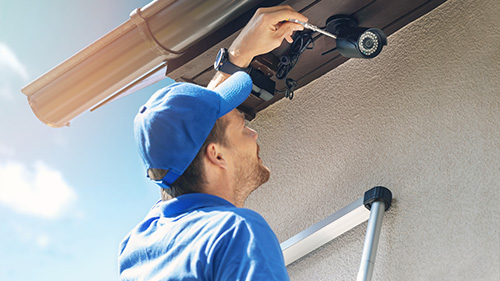 a man in a blue uniform installing a security camera on house