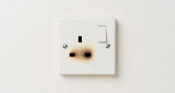 a burnt plug socket with cracked plastic on a white wall